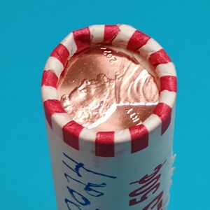 May include: A roll of pennies with a red and white striped edge. The end of the roll reveals a copper penny with the year 2017 visible. The roll is labeled with the year 2017 in blue ink.