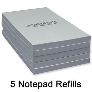 May include: Five white notepad refills stacked on top of each other. The top notepad has the text "LASERGRAM® CUSTOM ENGRAVED GIFTS" printed on it.
