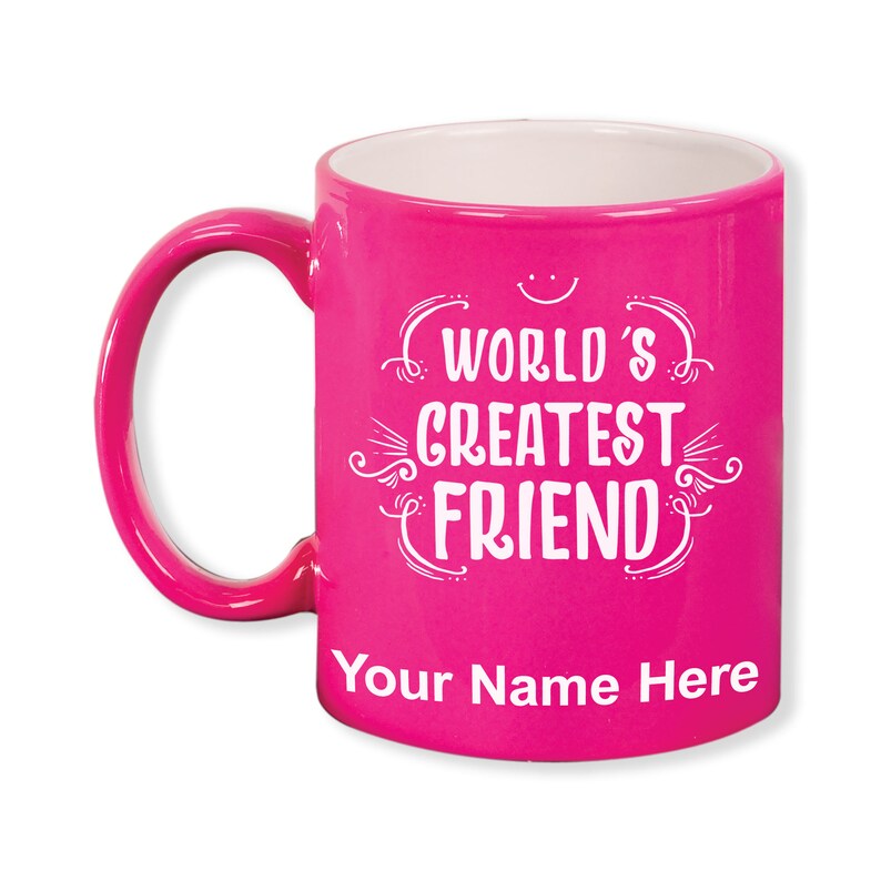 K&ouml;nnte beinhalten: Eine leuchtend pinkfarbene Keramiktasse mit wei&szlig;em Innenraum und einem gebogenen Henkel. Auf der Tasse steht in wei&szlig;er Schrift "WORLD'S GREATEST FRIEND", darunter Platz f&uuml;r eine Personalisierung. &Uuml;ber dem Text befindet sich ein Smiley.