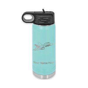 Puede incluir: Una botella de agua de acero inoxidable turquesa con tapa negra y asa de transporte. La botella tiene una silueta plateada de un avi&oacute;n de combate y el texto "Your Name Here" grabado en el lateral.