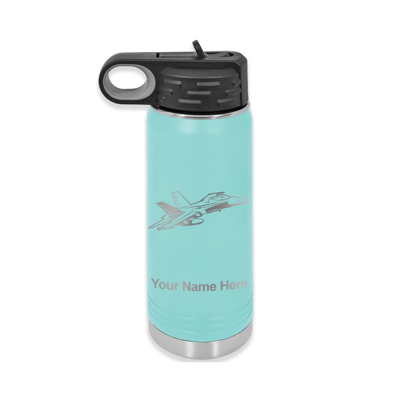 Puede incluir: Una botella de agua de acero inoxidable turquesa con tapa negra y asa de transporte. La botella tiene una silueta plateada de un avi&oacute;n de combate y el texto "Your Name Here" grabado en el lateral.