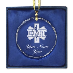 May include: A clear crystal ornament with a silver star of life and the letters EMT. The ornament is in a blue velvet box with a gold ribbon. The text "Your Name Year" is engraved on the ornament.