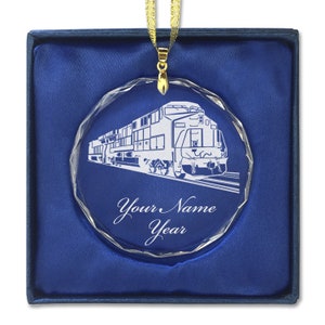 May include: A clear glass ornament with a detailed etching of a train engine. The ornament is in a blue velvet box and has a gold ribbon attached. The ornament also has the text "Your Name Year" etched on it.