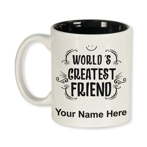 K&ouml;nnte beinhalten: Wei&szlig;er Keramikbecher mit schwarzem Innenraum und gebogenem Henkel. Der Becher zeigt den Text "WORLD'S GREATEST FRIEND" in dekorativer schwarzer Schrift, mit Platz f&uuml;r einen personalisierten Namen darunter.