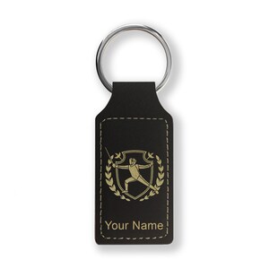 May include: Black leather keychain with a gold-colored fencing silhouette and laurel wreath design. The keychain has a silver key ring and the text "Your Name" is engraved on the bottom.