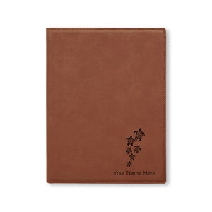 May include: Brown leather journal with a design of sea turtles and the text "Your Name Here" engraved on the front.