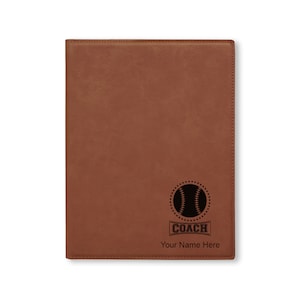 May include: Brown leatherette journal with a black baseball and the word "COACH" in a banner. The text "Your Name Here" is below the banner.