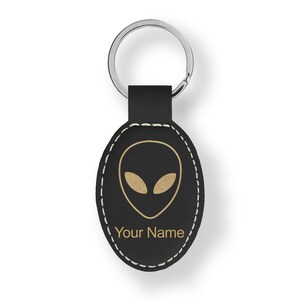 May include: Black leather keychain with a gold alien head design and the text "Your Name".
