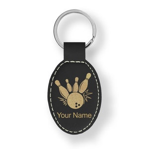 May include: Black leather oval keychain with a gold bowling ball and pins design. The keychain has a silver key ring and the text "Your Name" is engraved on the front.