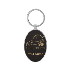 May include: Black oval keychain with a silver ring. The keychain features a gold outline of a hard hat, blueprint, and gears. The text "ENGINEERING" and "Your Name" are also in gold.