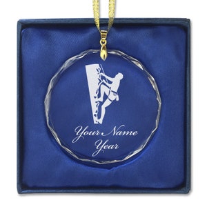 May include: A clear crystal ornament with a silhouette of a person rock climbing. The ornament is in a blue velvet box. The ornament is personalized with "Your Name Year".