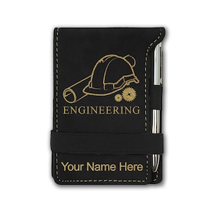 May include: Black leatherette notepad with a gold pen and a gold engraved design of a hard hat, blueprint, and gears. The text "ENGINEERING" is engraved below the design. The notepad has a black elastic band and the text "Your Name Here" is engraved below the band.