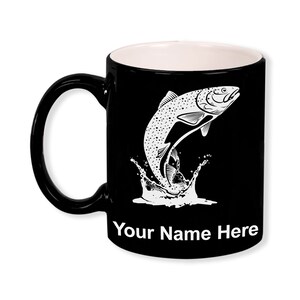 May include: Black ceramic mug with a white interior and handle. The mug features a white graphic of a leaping fish with water splashes. The text "Your Name Here" is printed in white at the bottom of the mug.