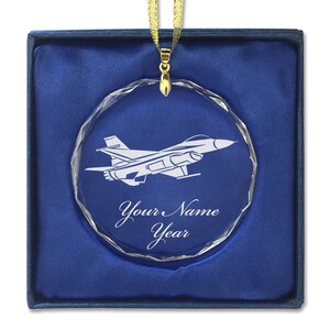 May include: A clear crystal ornament with a white outline of a fighter jet and the text "Your Name Year". The ornament is in a blue velvet box.