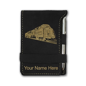 May include: Black notepad with a gold train graphic and the text "Your Name Here". The notepad has a black elastic band and a pen holder with a silver pen. The notepad is made of a textured material.