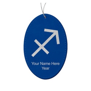 May include: A blue oval-shaped ornament with a silver Sagittarius symbol and the text "Your Name Here" and "Year". The ornament has a silver string for hanging.