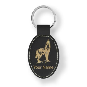 May include: Black leather keychain with a silver ring. The oval-shaped tag features a gold illustration of a howling wolf and the text "Your Name" in gold. The edges are stitched with white thread.