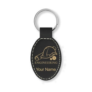 May include: Black leather oval keychain with a gold outline and stitching. The keychain features a gold graphic of a hard hat, blueprint, and gears with the text "ENGINEERING" and "Your Name".