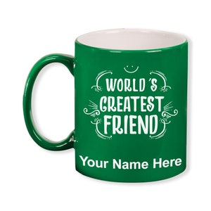 K&ouml;nnte beinhalten: Eine gr&uuml;ne Keramiktasse mit wei&szlig;em Innenraum und gr&uuml;nem Henkel. Die Tasse tr&auml;gt den wei&szlig;en Schriftzug "WORLD'S GREATEST FRIEND" mit Platz f&uuml;r einen personalisierten Namen darunter. Ein l&auml;chelndes Gesicht befindet sich &uuml;ber dem Text.