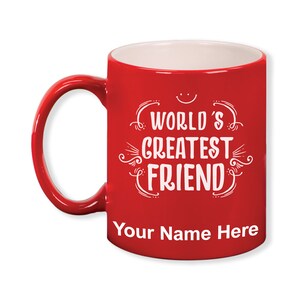 K&ouml;nnte beinhalten: Eine rote Keramik-Tasse mit wei&szlig;em Innenraum und Henkel. Die Tasse tr&auml;gt den Text "WORLD'S GREATEST FRIEND" in einer dekorativen Schriftart, mit Platz f&uuml;r einen personalisierten Namen unten. Ein l&auml;chelndes Gesicht befindet sich &uuml;ber dem Text.