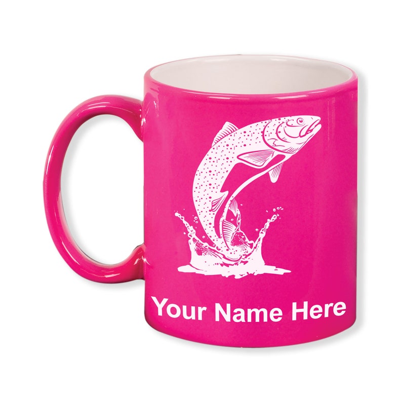 May include: A magenta ceramic mug with a white interior and handle. The mug features a white illustration of a fish leaping out of water. The text "Your Name Here" is printed below the fish design.