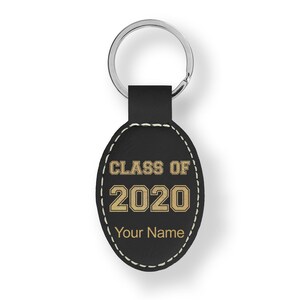 May include: Black leather keychain with a silver ring. The oval-shaped tag features the text "CLASS OF 2020" in gold lettering, with space for a name below. White stitching outlines the tag.