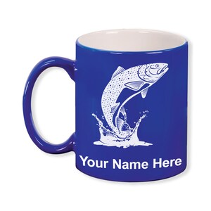 May include: A cobalt blue ceramic mug with a white interior and handle. The mug features a white graphic of a leaping fish with water splashes. The text "Your Name Here" is printed in white on the front.