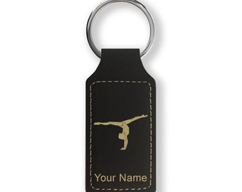 Op de afbeelding: Zwarte leren sleutelhanger met een gouden silhouet van een turnster die een handstand maakt. De sleutelhanger heeft een gestikte rand en de tekst "Your Name" is gegraveerd onder het silhouet.