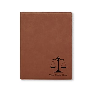 May include: Brown leatherette journal with a black scales of justice design and the text "Your Name Here".
