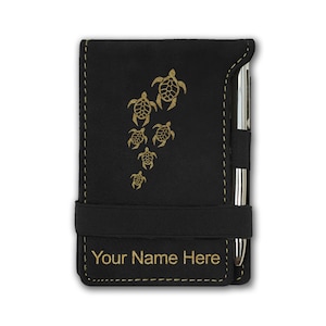 May include: Black leatherette notebook with a gold-colored design of sea turtles and a pen holder. The notebook has a black elastic band closure and the text "Your Name Here" is printed on the front.