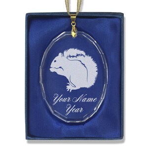 May include: A clear glass oval ornament with a white etched squirrel design. The ornament has a gold chain and is in a blue velvet box. The text "Your Name Year" is etched on the ornament.