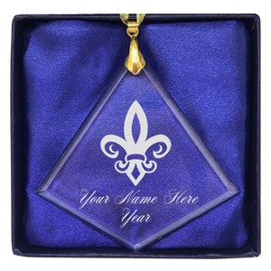 May include: A clear glass diamond-shaped ornament with a gold chain and a white fleur-de-lis design. The ornament has the text "Your Name Here Year" engraved on it.