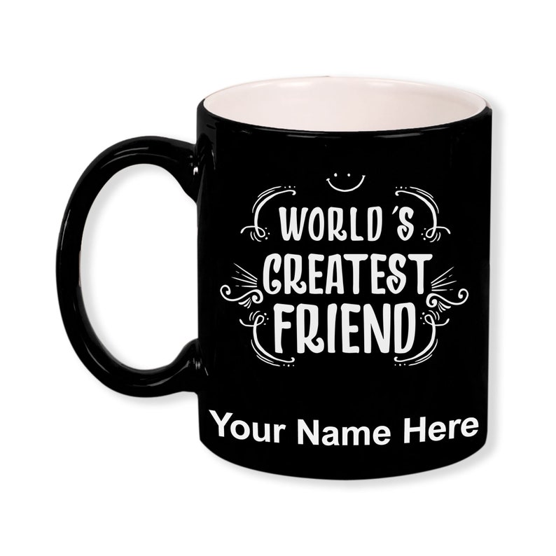K&ouml;nnte beinhalten: Schwarze Keramik-Tasse mit wei&szlig;em Innenraum und gro&szlig;em schwarzem Henkel. Die Tasse tr&auml;gt den wei&szlig;en Schriftzug "WORLD'S GREATEST FRIEND" mit Platz f&uuml;r einen personalisierten Namen unten.