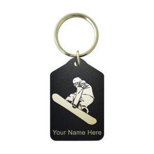 May include: Black metal keychain with a gold silhouette of a snowboarder. The keychain has a gold ring and the text "Your Name Here" is engraved on the bottom.