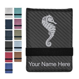 May include: A black carbon fiber wallet featuring a silver seahorse graphic and a black elastic band. The text Your Name Here is printed in silver at the bottom. A column of twelve additional wallets in various solid colors and textures is shown.