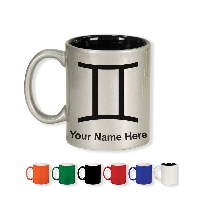 May include: A silver-colored mug with a black interior and handle. The mug features a black Gemini zodiac symbol and the text "Your Name Here". Several colorful mugs are displayed below.