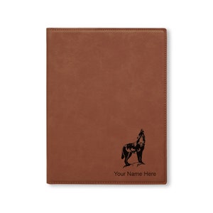 May include: A brown leather journal with a howling wolf graphic and the text "Your Name Here". The journal has a stitched border and a smooth, textured surface. The wolf is black.