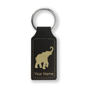 May include: Black leather keychain with a silver ring. The keychain features a gold elephant silhouette and the text "Your Name" in a serif font. The edges are stitched with a light-colored thread.