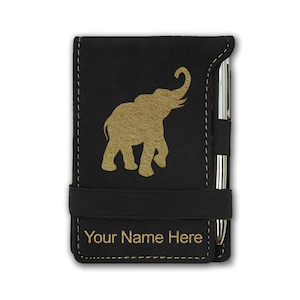 May include: Black leatherette notebook with a gold elephant silhouette and a pen holder. The notebook has a black elastic band closure and the text "Your Name Here" is embossed on the front.