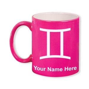 May include: A bright pink ceramic mug with a white interior and handle. The mug features the Gemini zodiac symbol in white and the text "Your Name Here" at the bottom. The mug is designed for hot beverages.