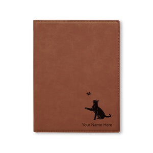 May include: Brown leather journal with a black silhouette of a cat chasing a butterfly. The journal has the text "Your Name Here" engraved on the front.