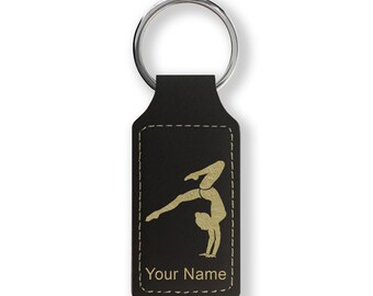 Op de afbeelding: Zwarte leren sleutelhanger met een zilveren ring. De sleutelhanger heeft een goudkleurig silhouet van een turnster in een handstand. De tekst "Your Name" is in goud onder de turnster afbeelding gedrukt. De randen zijn gestikt met lichtgeel garen.