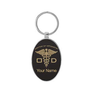 May include: A black oval keychain with a silver ring. The keychain features a gold medical symbol with the letters "OD" and the text "Doctor of Optometry". The text "Your Name" is also included on the keychain.