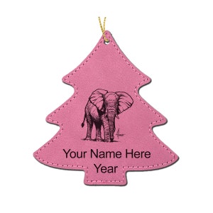 May include: A pink Christmas tree ornament with a detailed black illustration of an elephant. The ornament has the text "Your Name Here" and "Year" at the bottom. A gold string is attached for hanging.