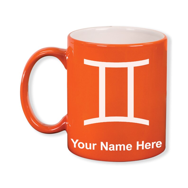 May include: Orange ceramic mug with a white Gemini symbol and the text "Your Name Here." The mug has a white interior and a curved handle. The mug is a vibrant orange color.