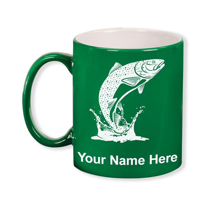 May include: A green ceramic mug with a white interior and handle. The mug features a white illustration of a fish leaping out of water, with the text "Your Name Here" at the bottom. The mug is designed for beverages.