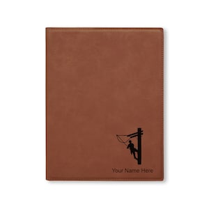 May include: Brown leatherette journal with a silhouette of a lineman working on a power pole. The journal has the text "Your Name Here" printed on the bottom.