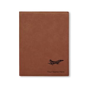 May include: Brown leatherette journal with a black silhouette of a fighter jet and the text "Your Name Here" engraved on the front.