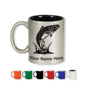 May include: A silver ceramic mug with a black interior and handle. The mug features a black graphic of a fish leaping out of water, with the text "Your Name Here" below. Several colored mugs are displayed below.
