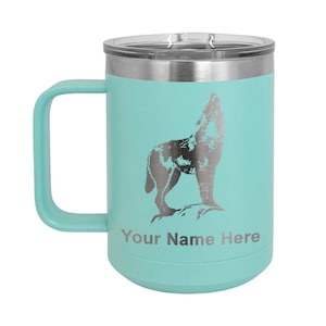 May include: A teal stainless steel travel mug with a wolf howling design and a silver lid. The mug has a handle and the text "Your Name Here" is printed on the bottom.